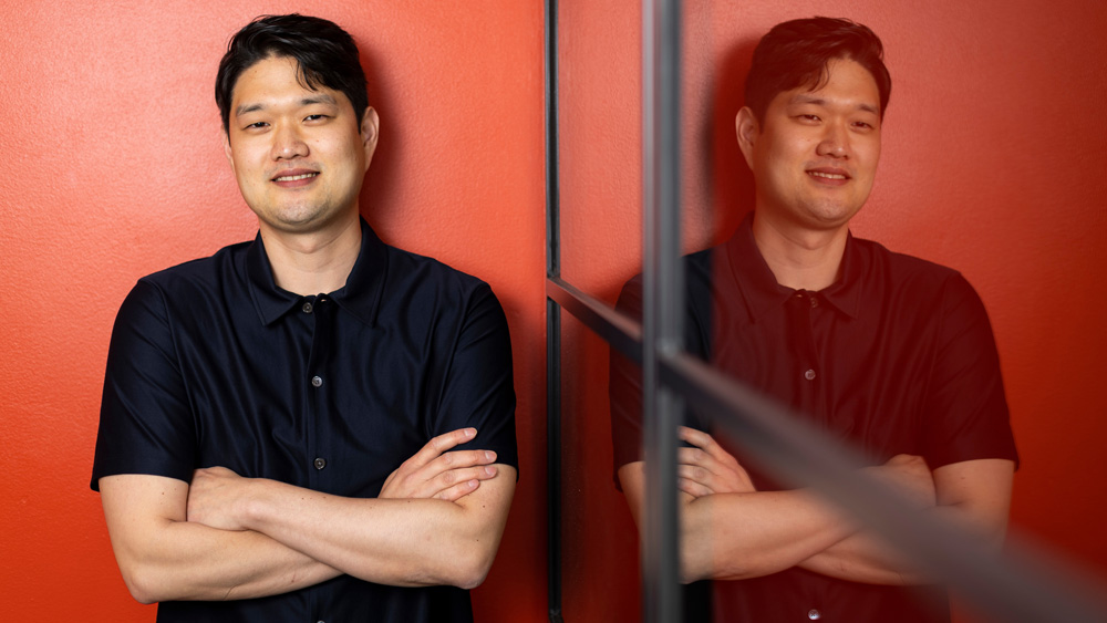 Photo of Jungwoo Chun with red wall in background, and Chun's reflection in glass wall
