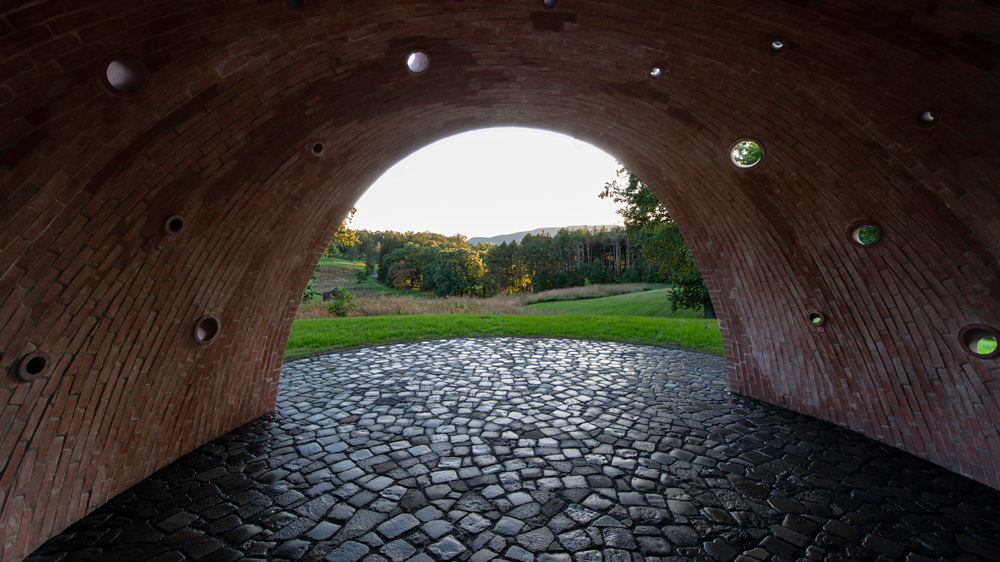  A view of green countryside seen through the arched entrance of the brick sculpture
