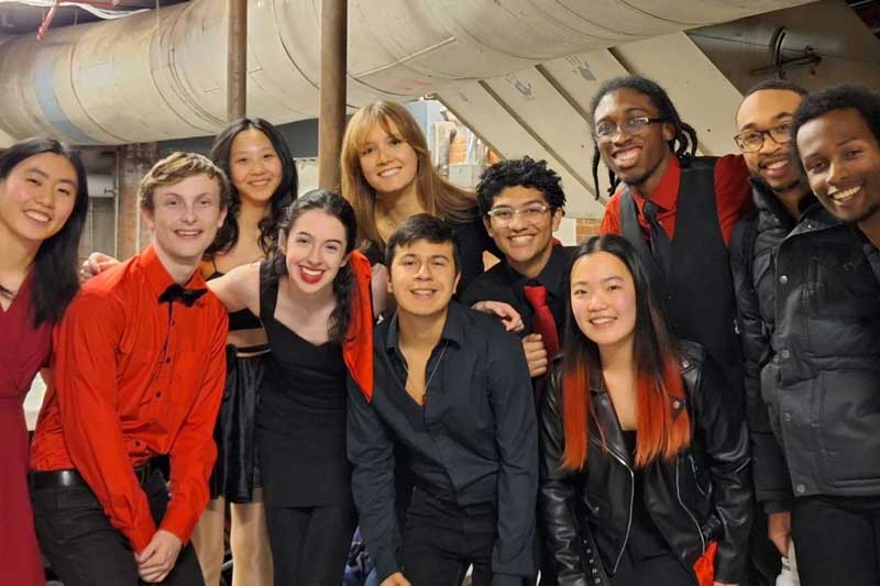 11 singers pose for a group photo, wearing black and red
