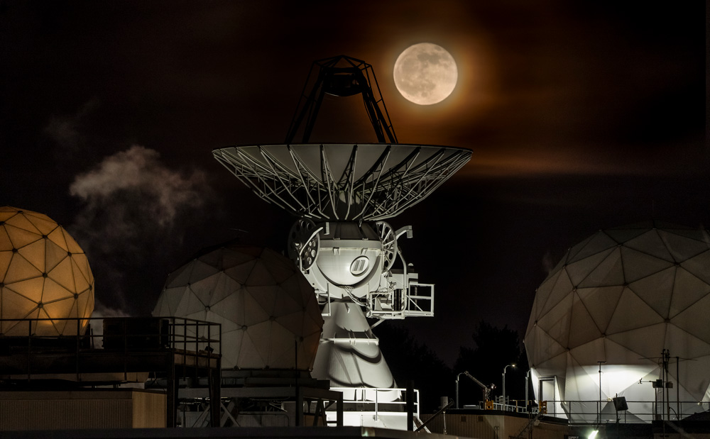 A huge radar and 3 spherical radomes of the Lincoln Lab at night, with full moon.