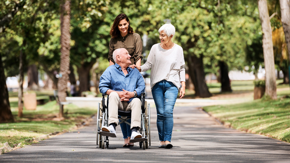Elderly man in wheelchair on a walk with 2 people