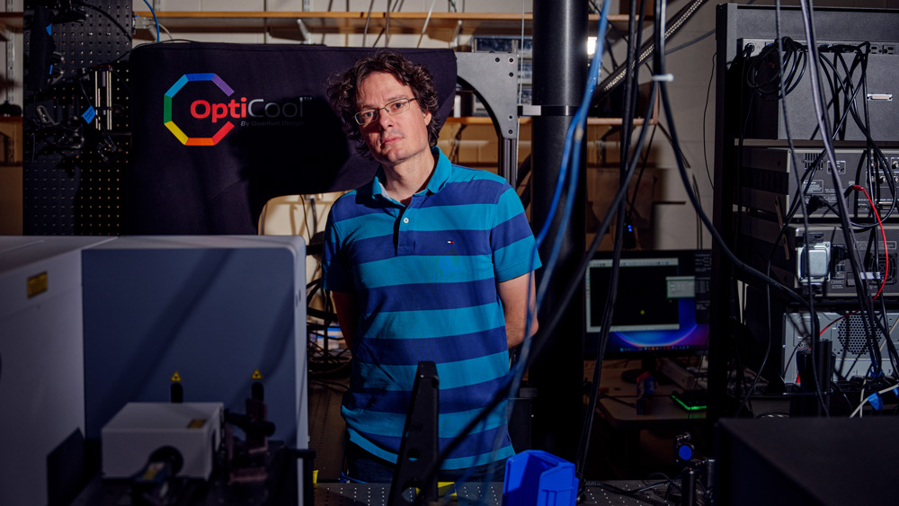 Riccardo Comin stands in the lab filled with cables and large equipment